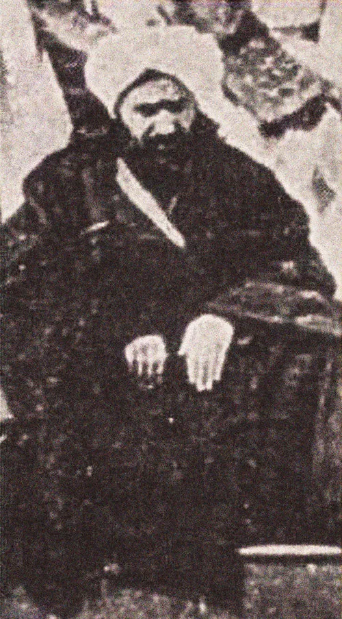 A portrait of Abu Bakr Effendi in a turban and dark robe, a serious bearded man of the nineteenth century.