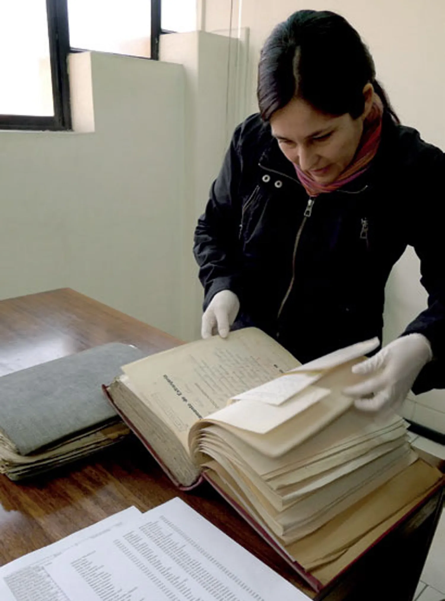An archivist, Karin Pereira Contardo, sits at a wooden desk reading old Ottoman-era immigration records at the Chilean National Archive.