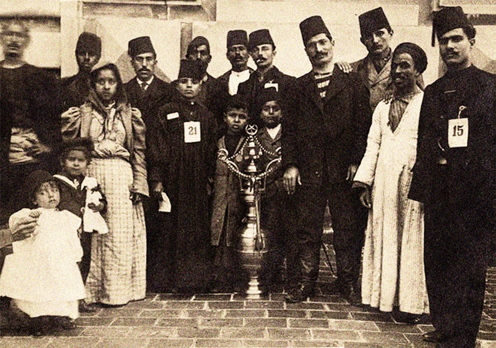 A black-and-white studio photograph of a group of Ottoman immigrants, men and women in dark Western clothes, arranged in two rows.