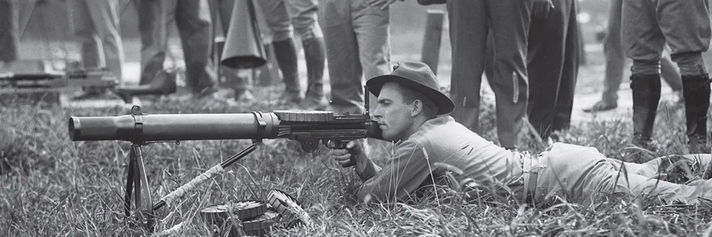 A black-and-white photograph of soldiers practising with machine guns before the emu hunt, watched by a group of farmers.