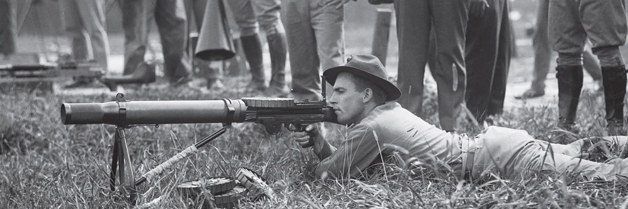 A black-and-white photograph of soldiers practising with machine guns before the emu hunt, watched by a group of farmers.