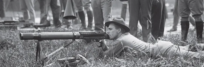 A black-and-white photograph of soldiers practising with machine guns before the emu hunt, watched by a group of farmers.
